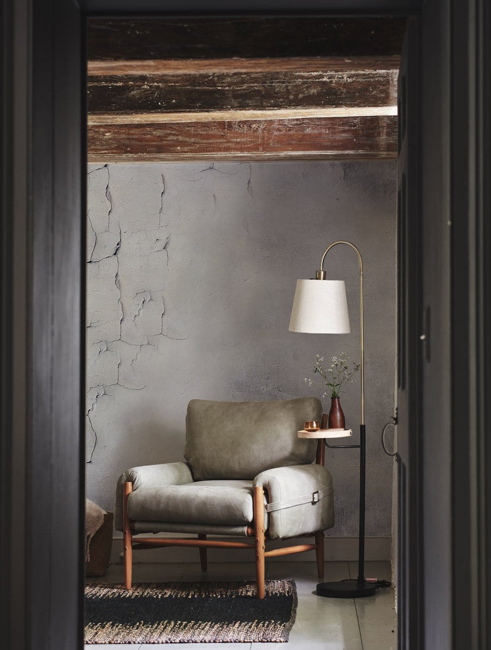 Vintage industrial concrete grey wallpaper mural with armchair, floor lamp, and wooden ceiling beams.