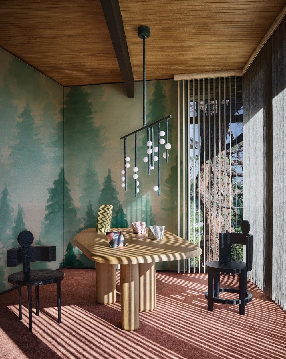 Misty Forest Green Watercolour Wallpaper in cosy dining room with modern table, black chairs, pendant light.