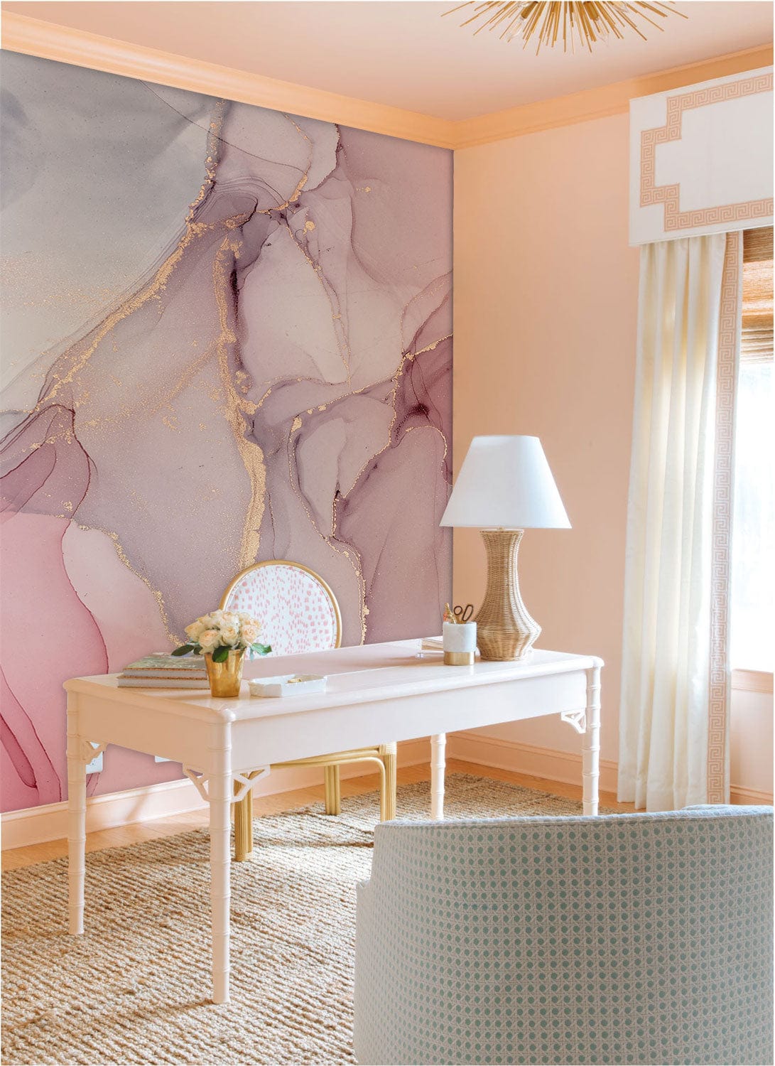 Elegant desk with lamp, gold accents, and pink marble-effect mural; woven rug adds texture.
