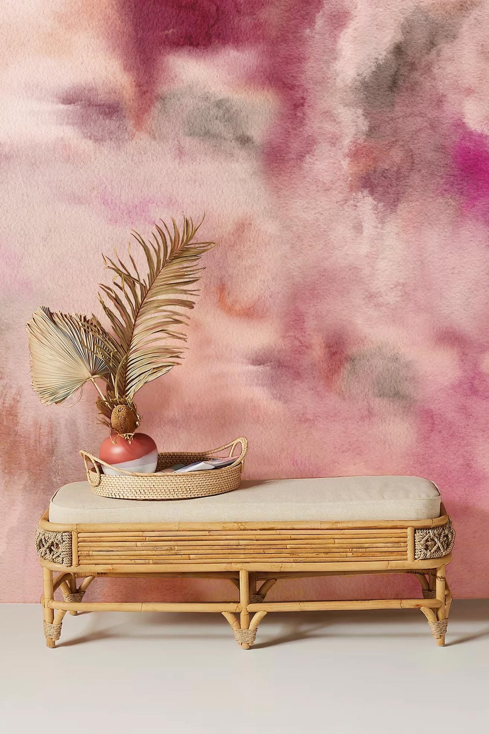 Dreamy mural wallpaper in pink and beige, rattan bench, soft neutral flooring, abstract cloud design.