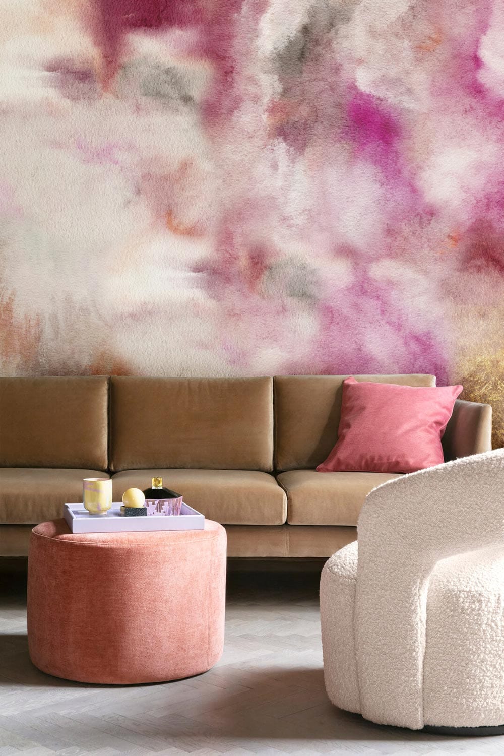Dreamy Watercolour Mural Wallpaper with soft pink and beige clouds, brown sofa, and pink ottoman.
