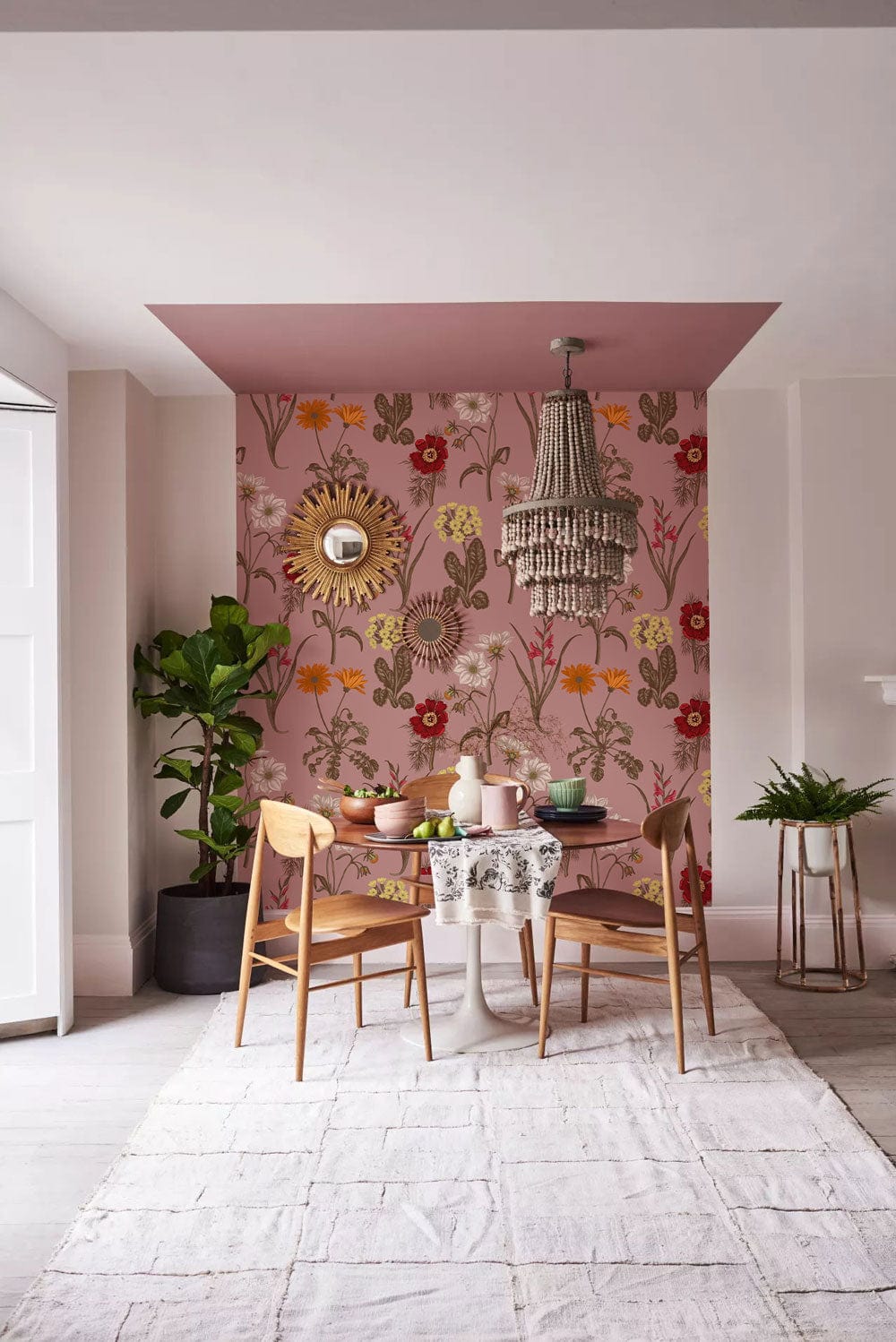Vintage floral wallpaper with warm red tones, wooden chairs, round table, rug, and stylish chandelier.