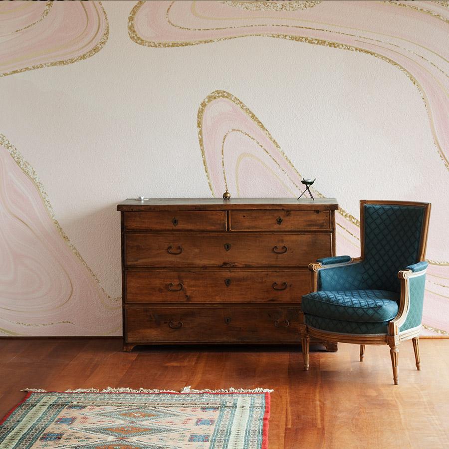 Elegant pink marble mural with glitter accents, wooden chest, teal armchair, and hardwood floor in room.