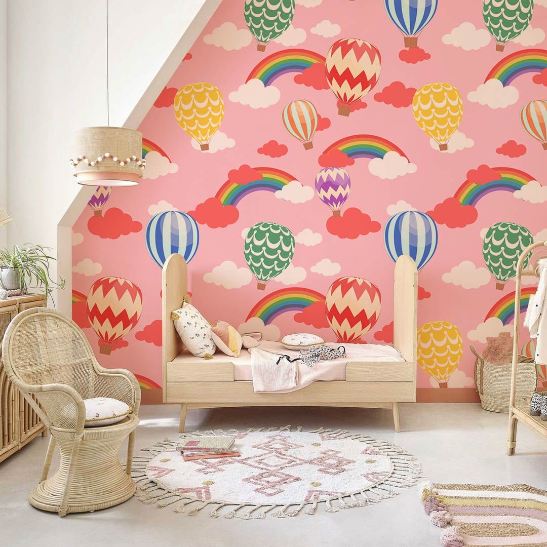 Colourful hot air balloon and rainbow wallpaper mural in children's bedroom with rattan chair and rug.