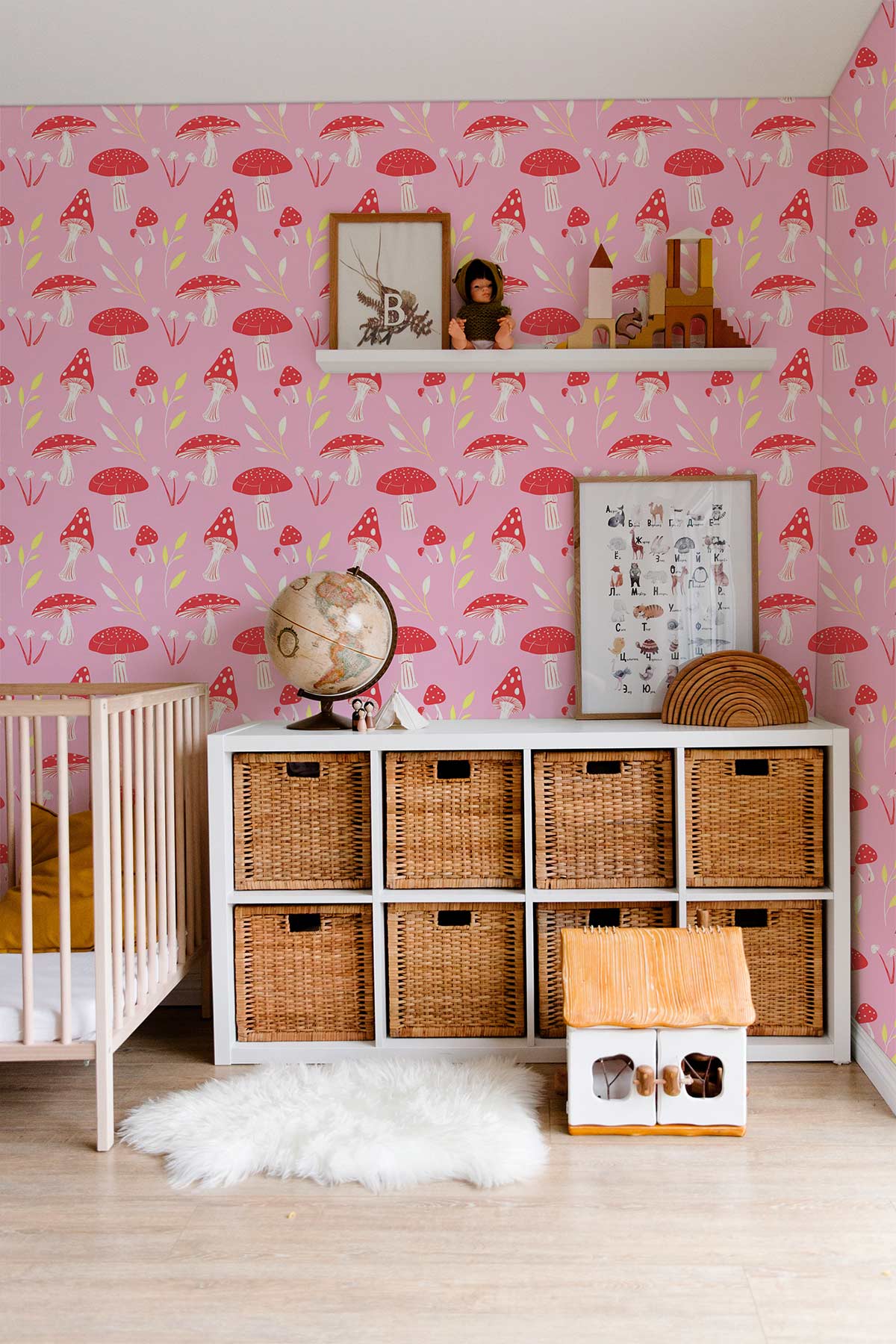 Charming pink mushroom wallpaper in cosy children's room; wicker storage, crib, light wood floor, decor accents.
