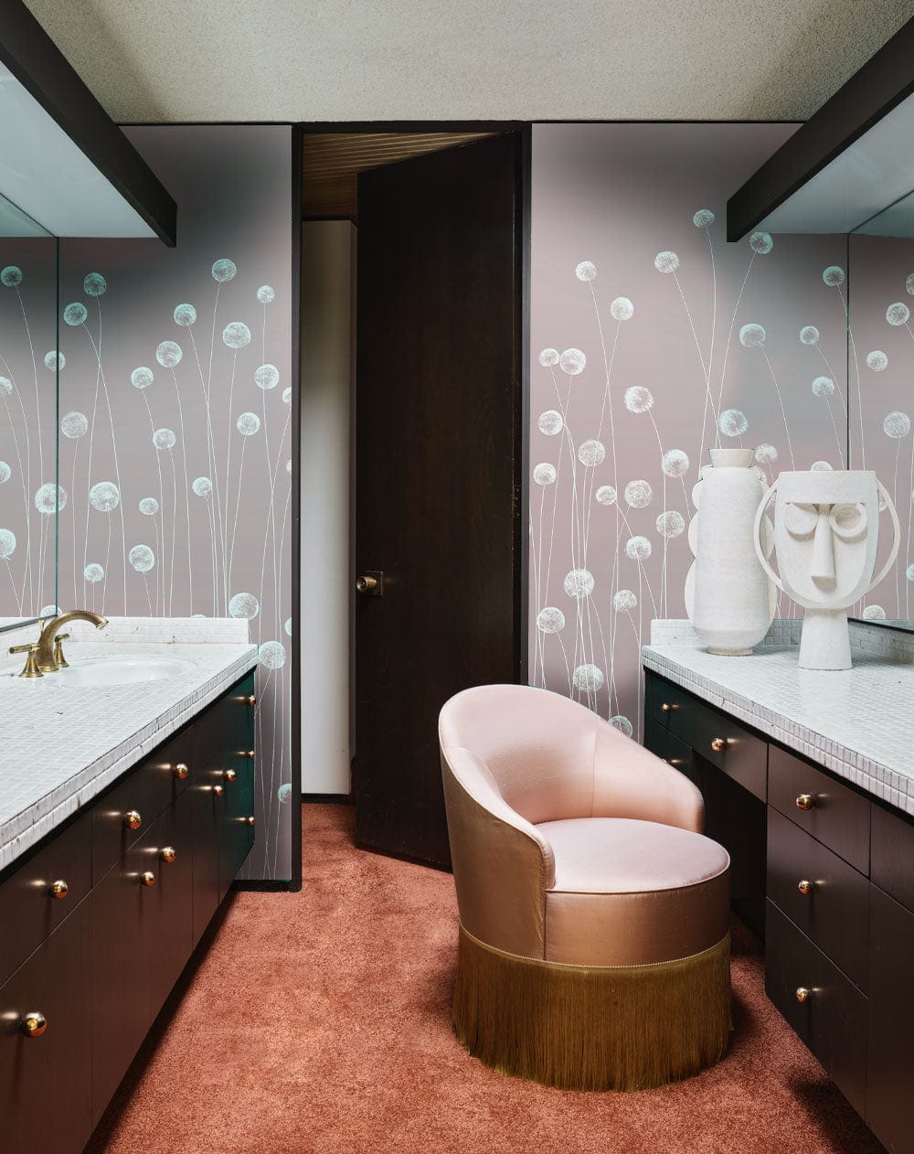 Soft pink wildflower mural wallpaper in elegant bathroom with brown cabinetry and plush pink chair.