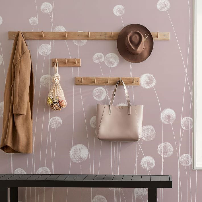 Soft pink wildflower mural wallpaper with wooden coat rack, beige jacket, hat, and handbag decor.