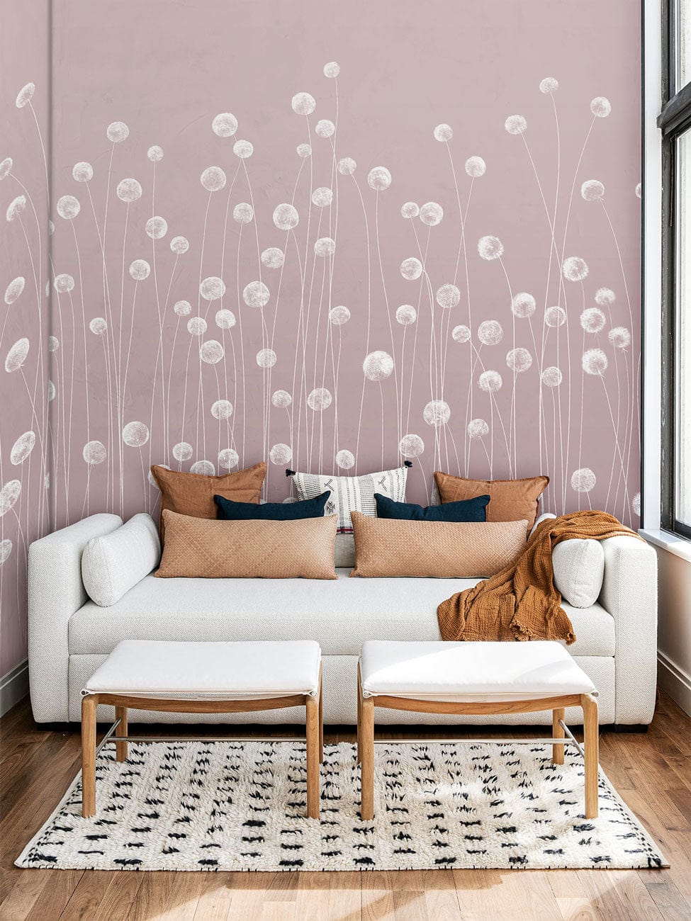 Soft pink wallpaper with wildflower design, white sofa, patterned rug, wooden flooring in living room.