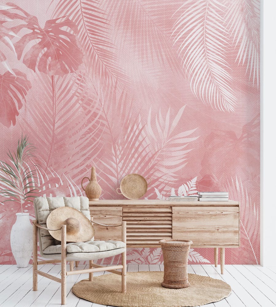 Blush pink tropical foliage wallpaper, wooden sideboard, woven decor items, neutral chair, white flooring.