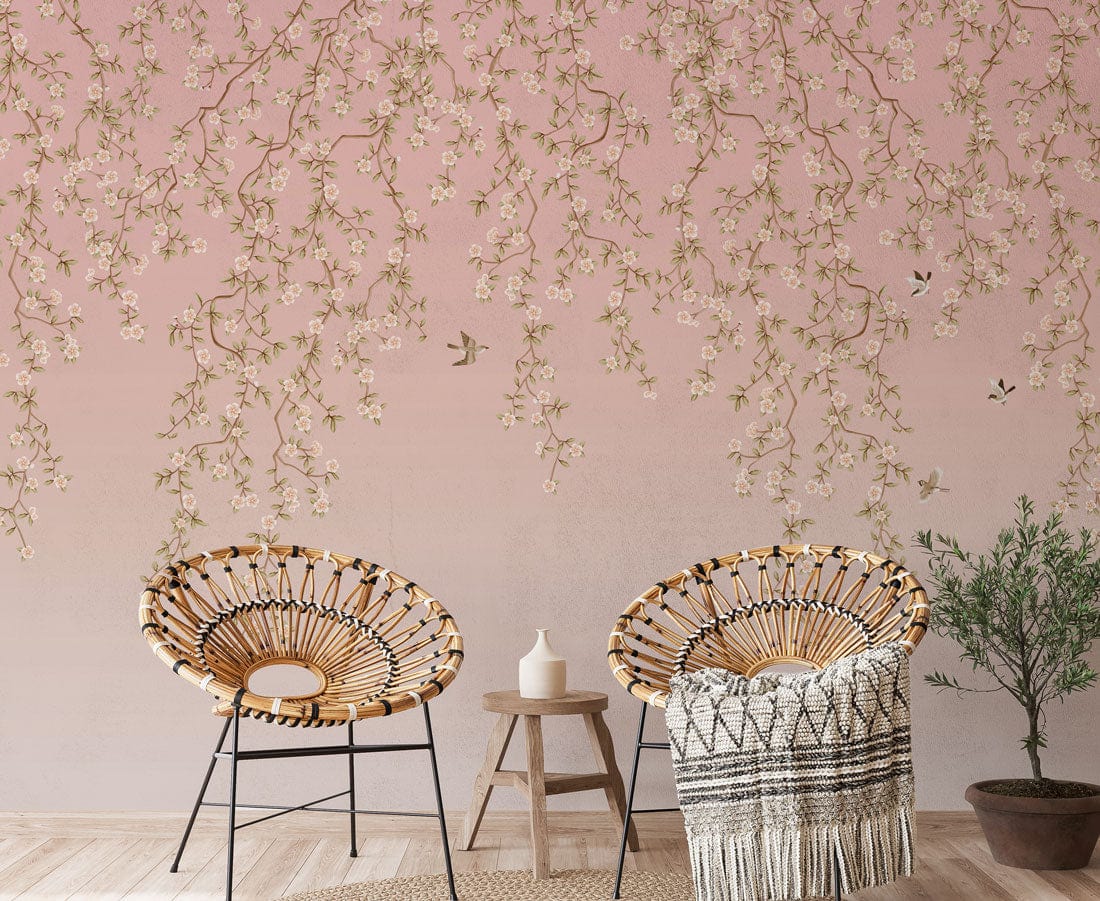 Blossoming pink floral mural wallpaper with birds, wicker chairs, wooden flooring in cosy room setting.
