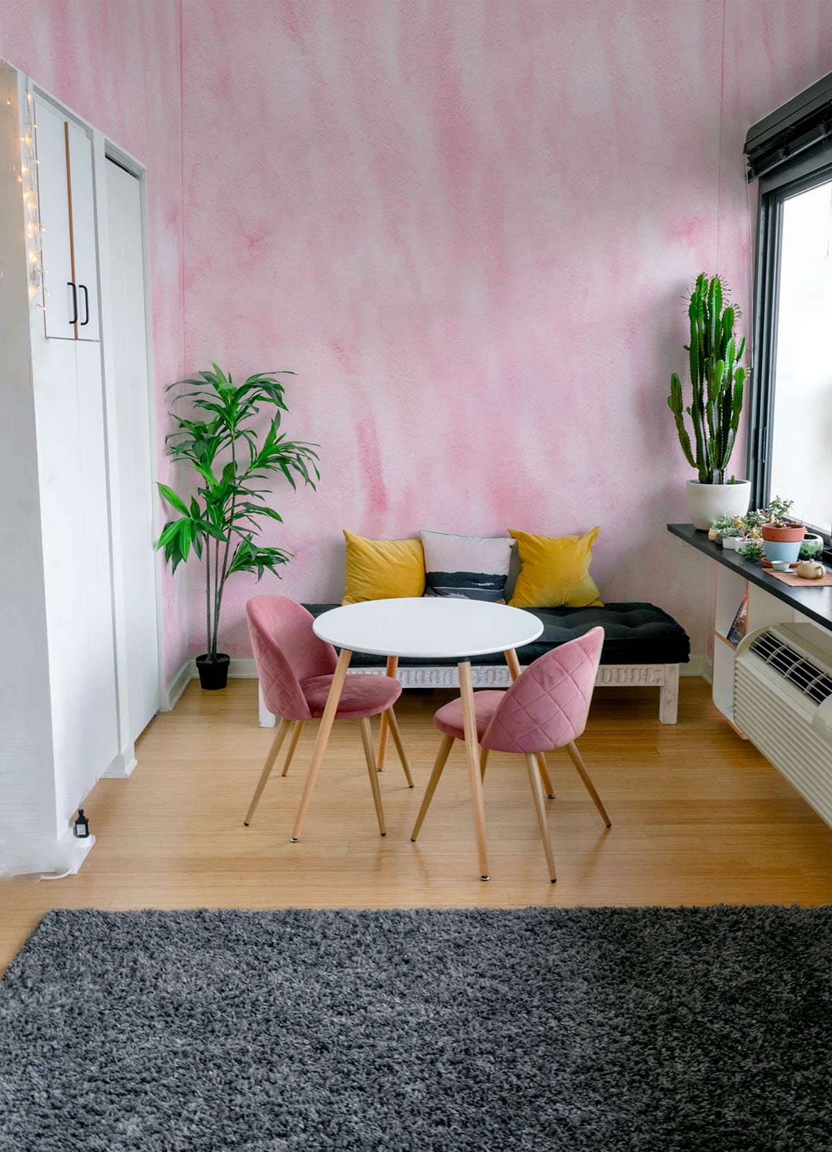 Soft pink watercolour texture mural wallpaper in living room with modern chairs and grey rug.