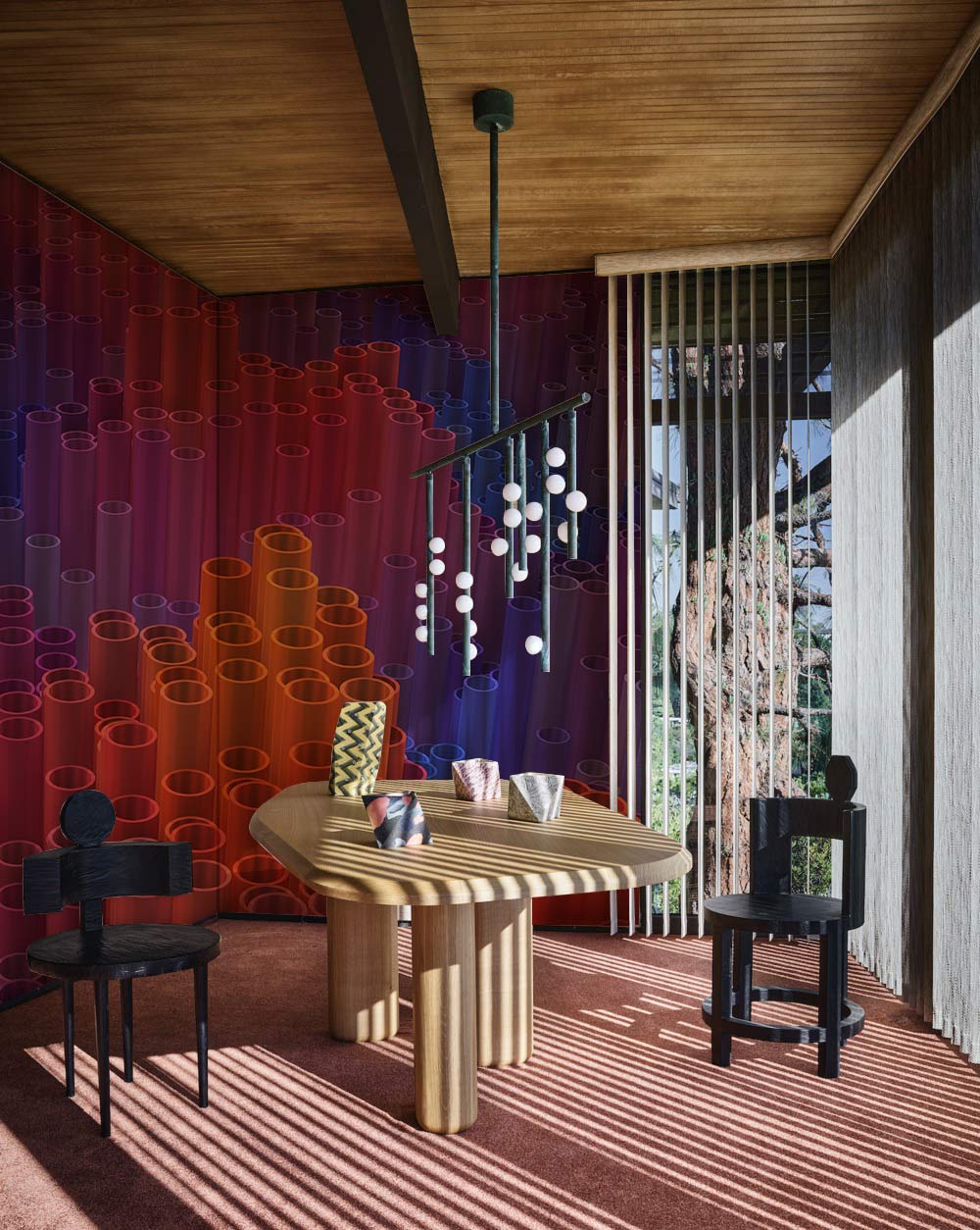 Vibrant abstract wall mural in dining room with wooden ceiling, striped table, black chairs, pendant light.