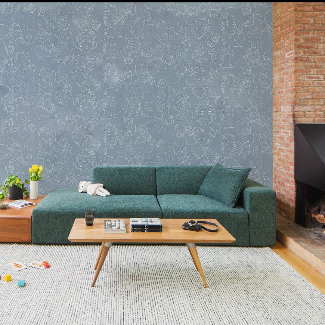 Elegant blue abstract faces wallpaper; green sofa, hardwood floor, white rug, brick wall, living room.