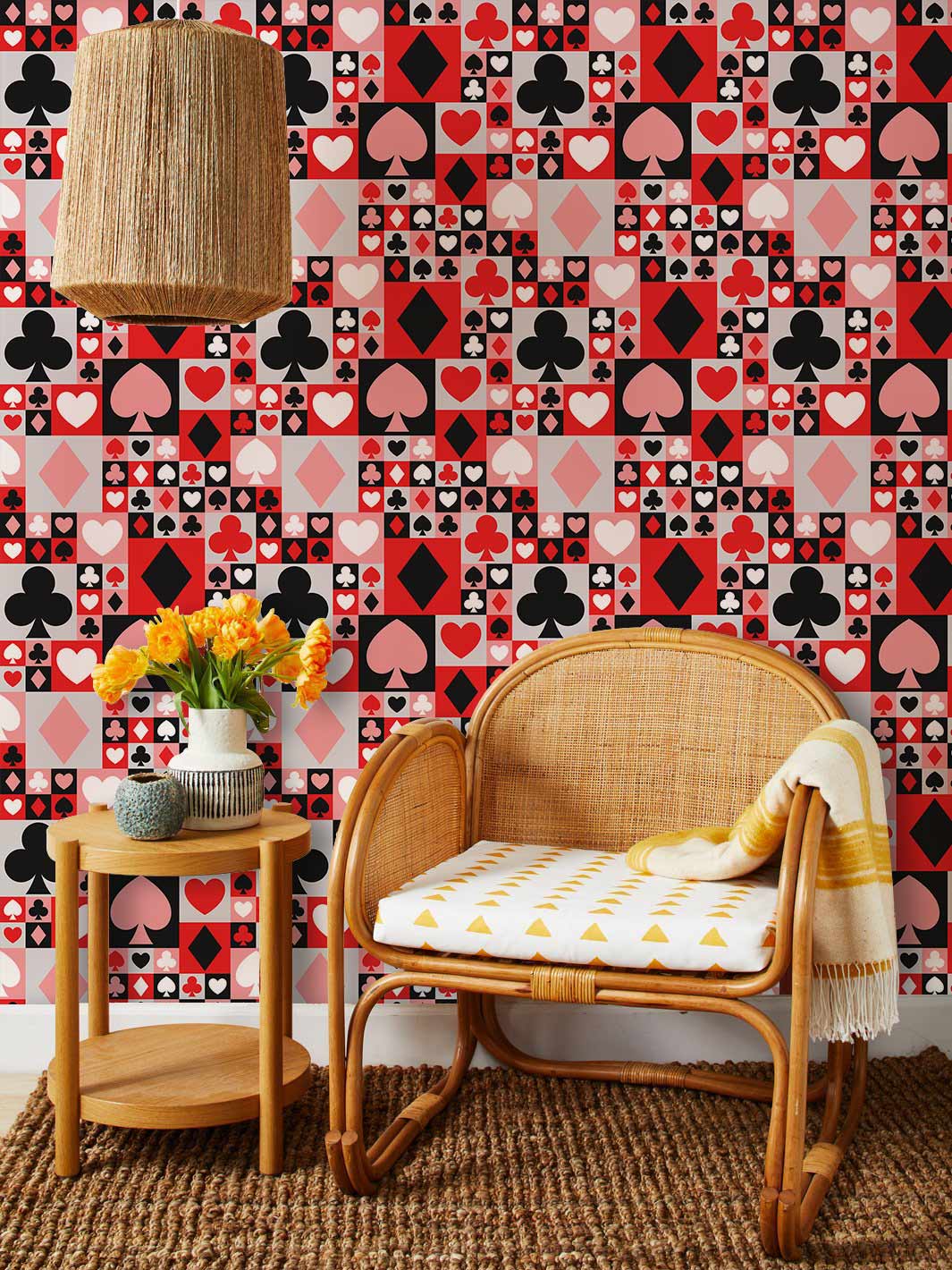 Retro playing card wallpaper in red, black, and pink with rattan chair, wicker lamp, woven rug.