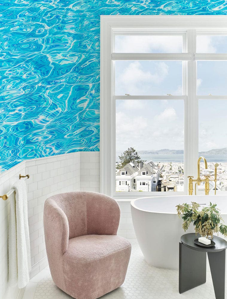 Vivid Aqua Blue Water Ripple Wallpaper in luxurious bathroom with pink chair, white bathtub, coastal view.