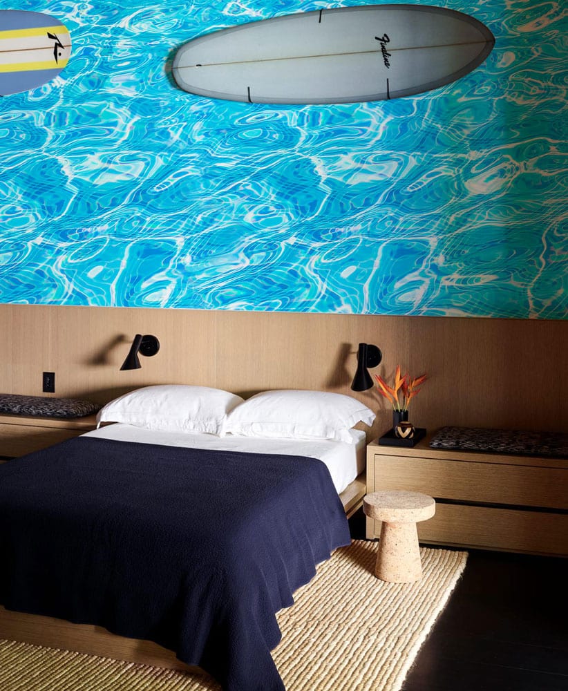 Vivid Aqua Blue Water Ripple Wallpaper in bedroom with mid-century furniture, wooden accents, and surfboard decor.