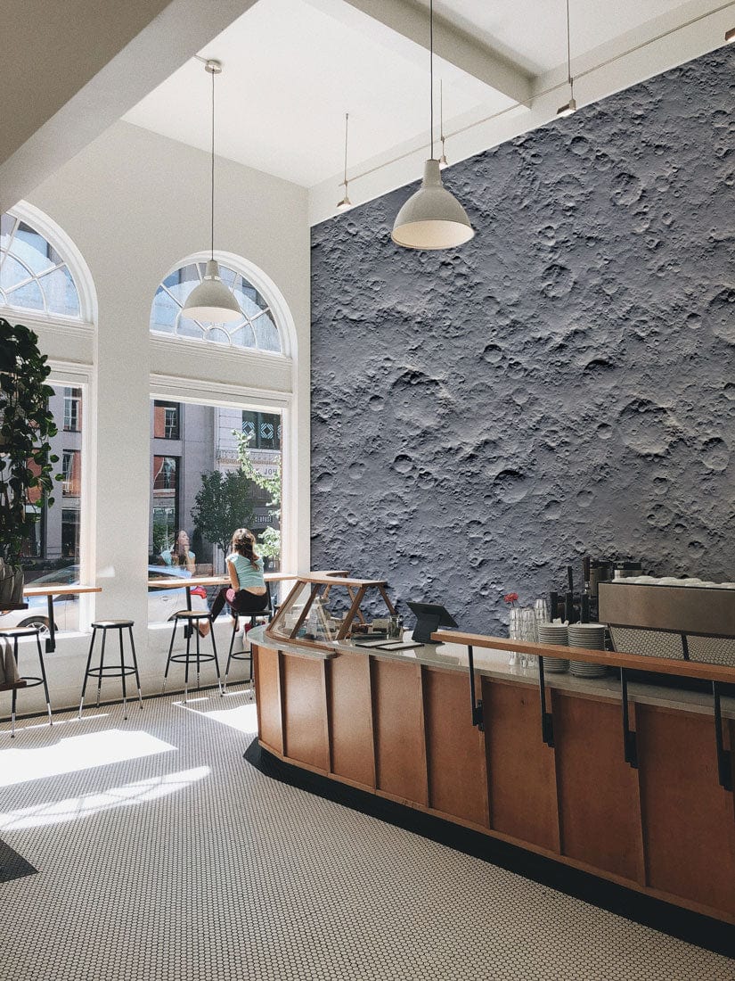 Lunar Surface Grey Textured Wallpaper in café with arched windows, bar stools, wood counters, hanging lights.