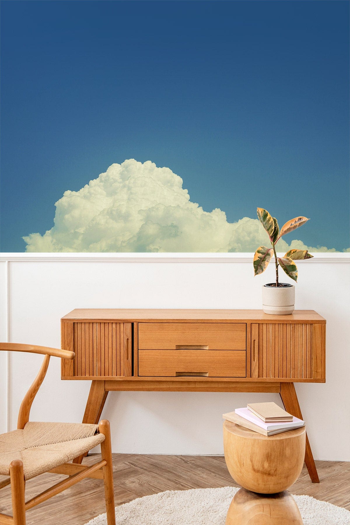 Ethereal mural wallpaper with cloud design, wooden sideboard, woven chair, parquet flooring in living room.