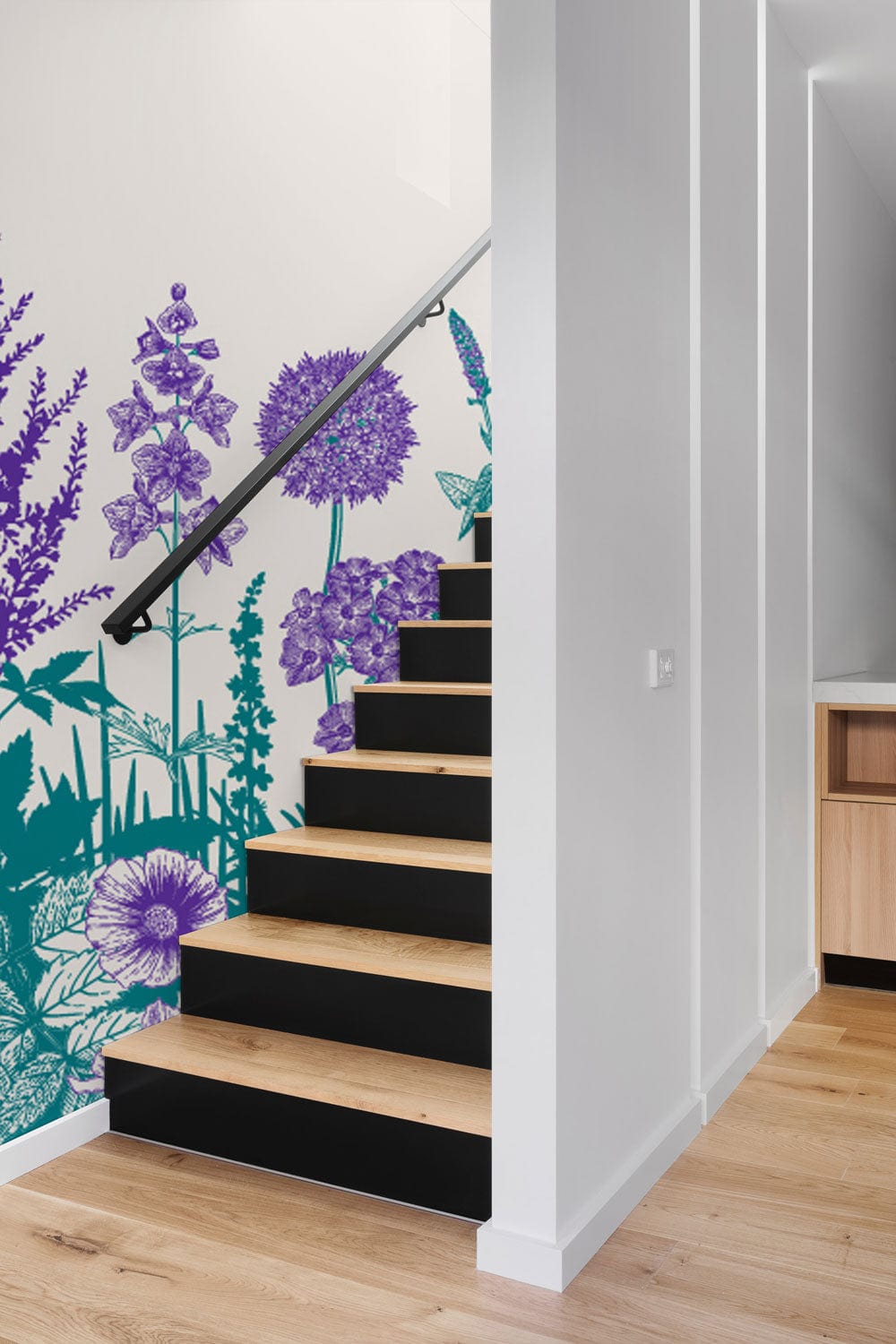 Modern hallway featuring floral wallpaper, black staircase, wooden flooring, and white walls.