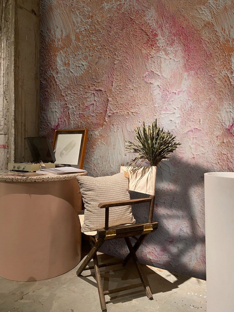 Textured blush pink abstract mural wallpaper, wooden chair, cream cushion, round table, rustic style.
