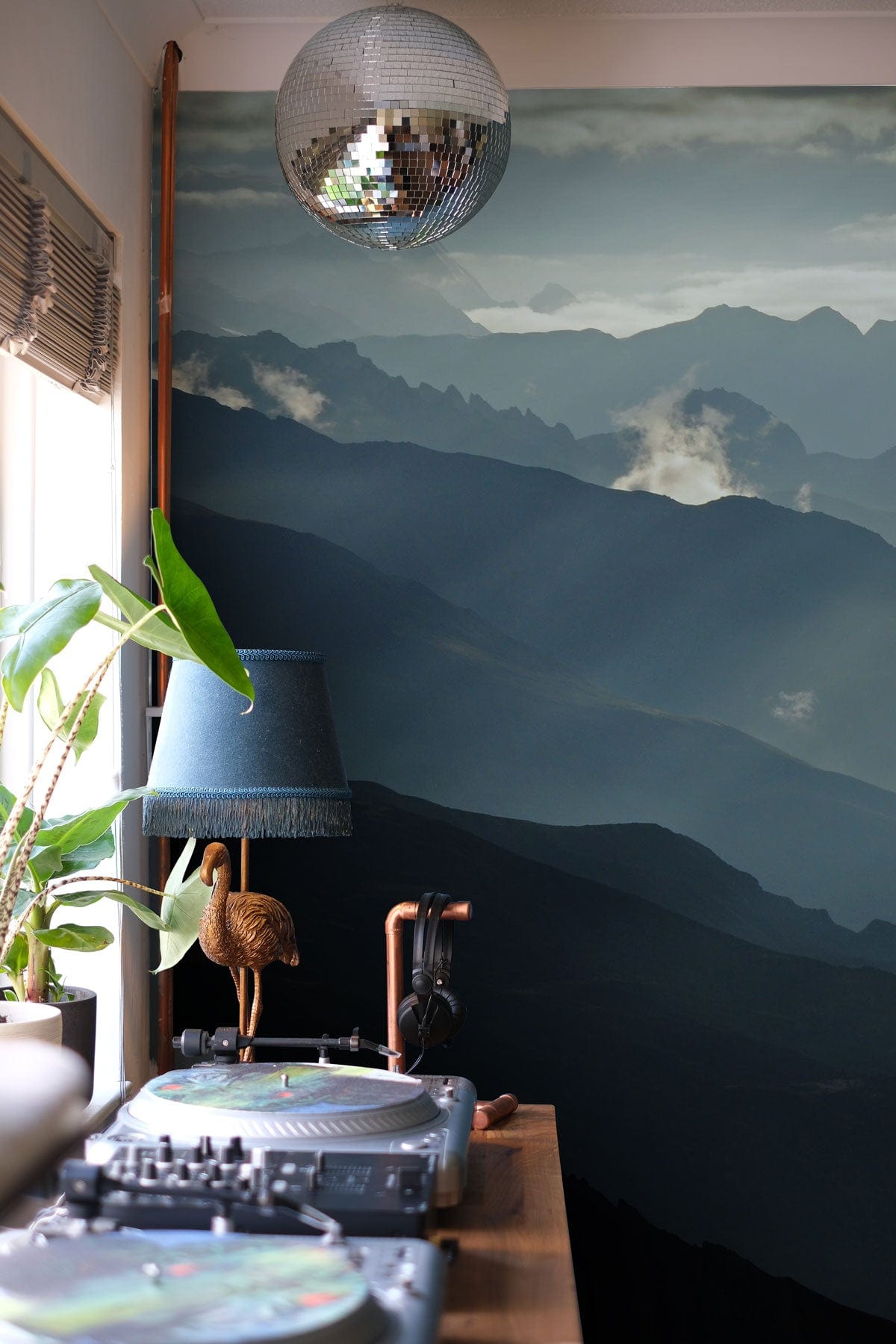 Serene mountain landscape mural in moody blue tones with disco ball and lamp in living room.