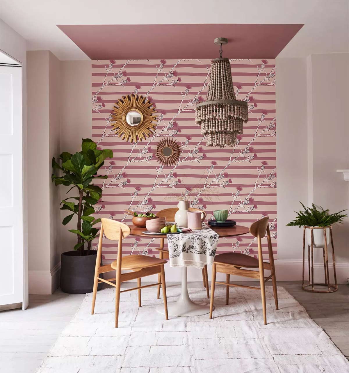 Vintage blush floral wallpaper in dining room with wooden chairs, light rug, and statement chandelier.