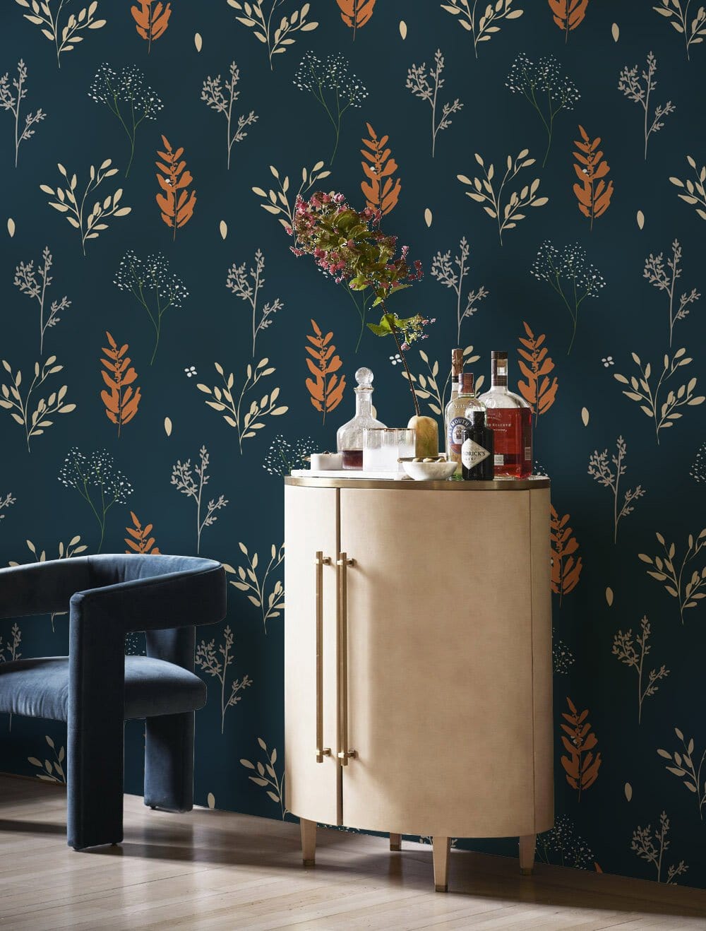 Vintage botanical wallpaper in teal and orange with beige cabinet and blue velvet chair, wooden floor.