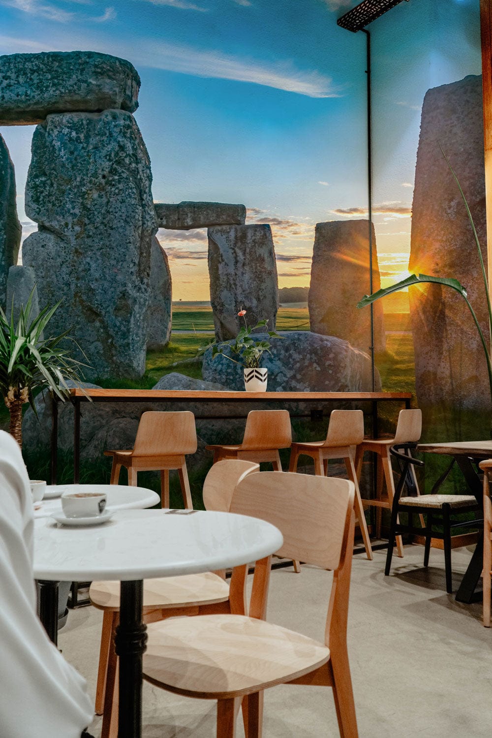 Sunlit Stonehenge Scenic Mural Wallpaper in café with wooden chairs, marble tables, and industrial lighting.