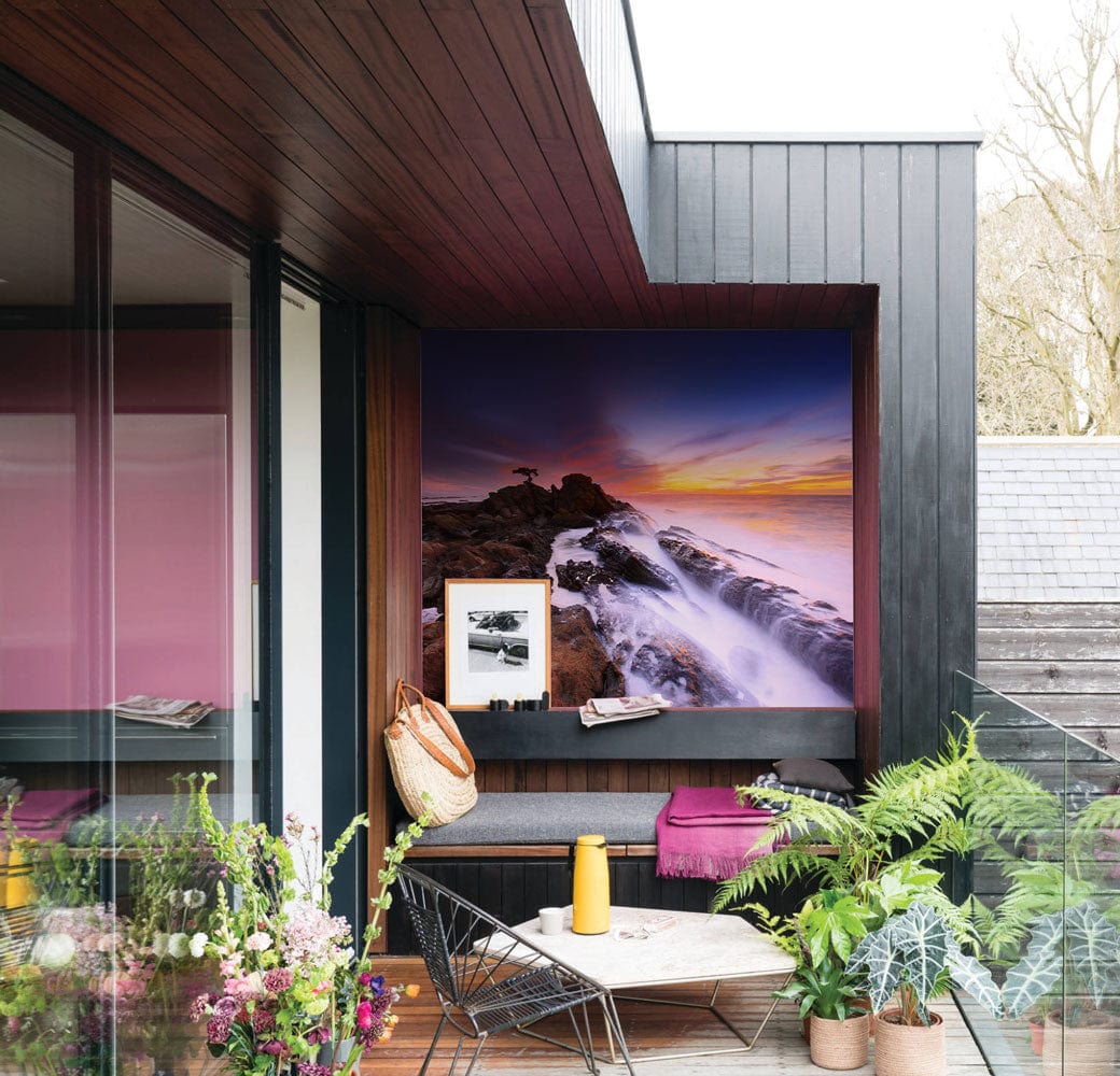 Sunset Seascape Mural Wallpaper in vibrant colours, outdoor seating, contemporary patio with plants, cosy alcove.