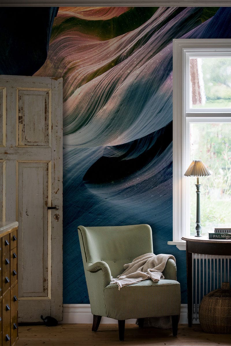Luxurious mural wallpaper, blue and peach, complements sage armchair, rustic door, wooden flooring.