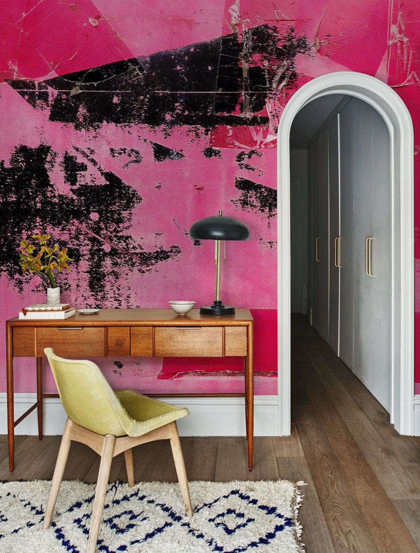 Vibrant pink graffiti wallpaper with desk, arched doorway, wooden flooring, and beige chair in modern room.