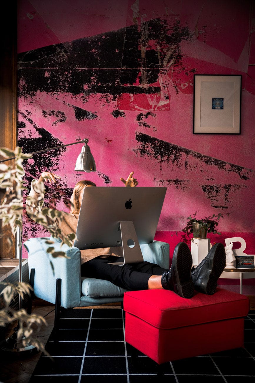 Vibrant pink graffiti wallpaper, blue armchair, black grid flooring, modern wall art, red ottoman, workspace.