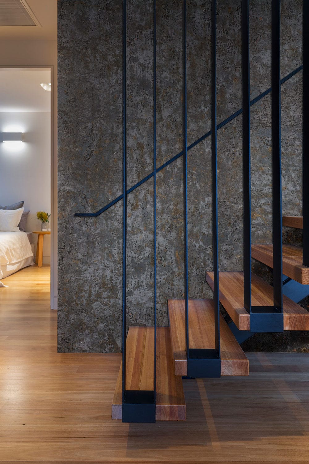 Rustic industrial charcoal wallpaper behind modern staircase in contemporary home interior with wooden flooring.