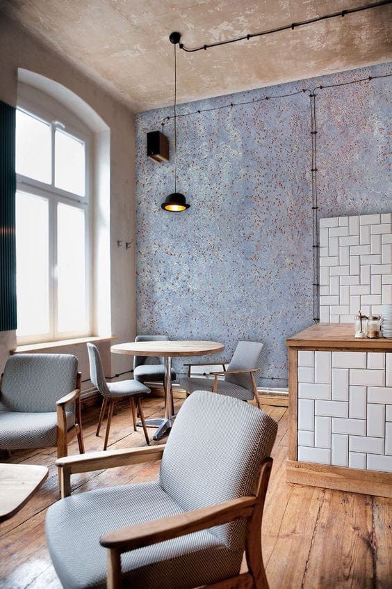 Rustic blue weathered metal effect wallpaper; light grey armchairs; wooden flooring; industrial-style dining room.