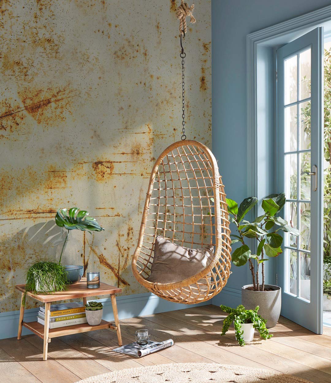 Rustic mural wallpaper with hanging chair, earthy tones, wooden side table, light blue wall, indoor plants.