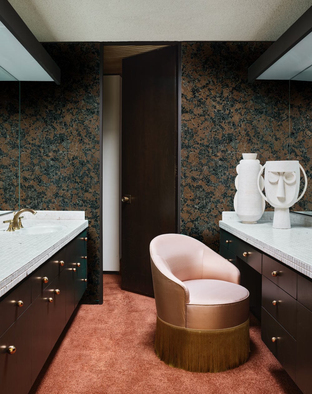 Luxurious bathroom with rustic granite effect wallpaper; plush pink chair; stylish vanity units.