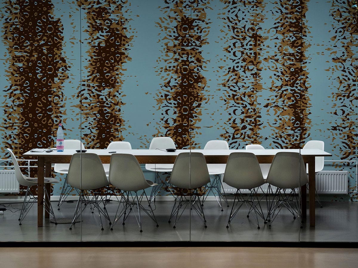 Rustic teal and brown ornate wallpaper in dining room with white chairs, wooden table, mirrored floor.