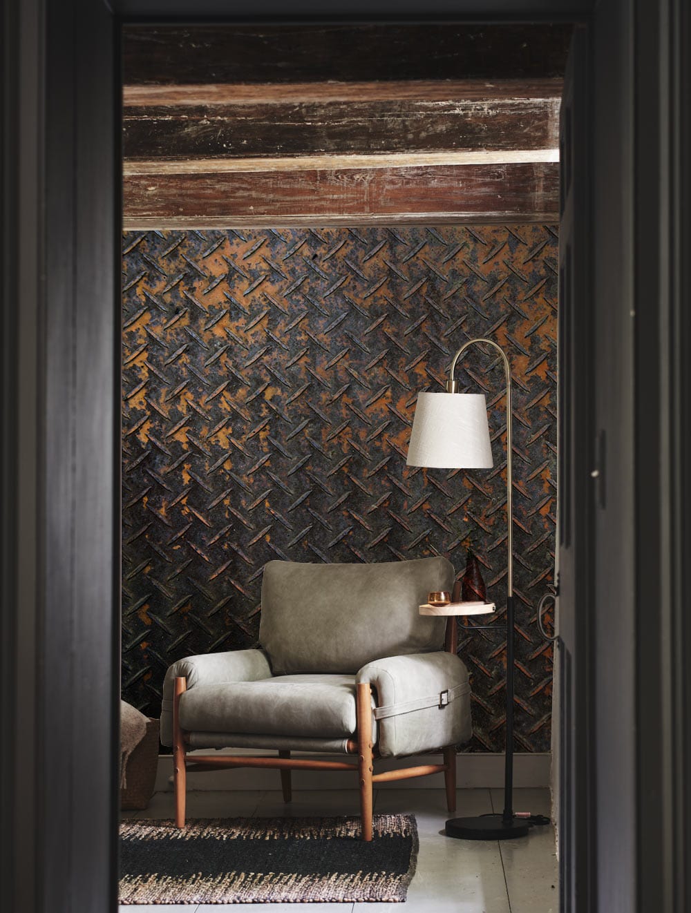 Industrial Rust Metallic Mural Wallpaper, weathered brown-black, grey armchair, floor lamp, cosy living room.