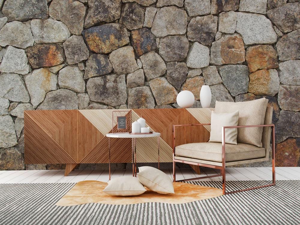 Rustic stone wall wallpaper mural in sitting room with geometric sideboard, modern armchair, striped rug.