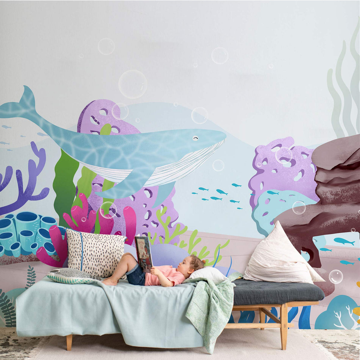 Children's ocean-themed wall mural with blue whale, pastel decor, cosy sofa in a playroom setting.