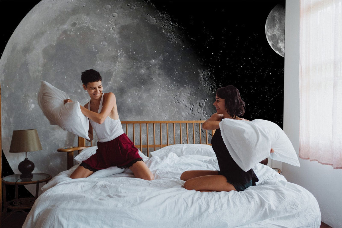Galaxy Journey: Monochrome lunar mural wallpaper behind bed in cosy bedroom with wooden accents.