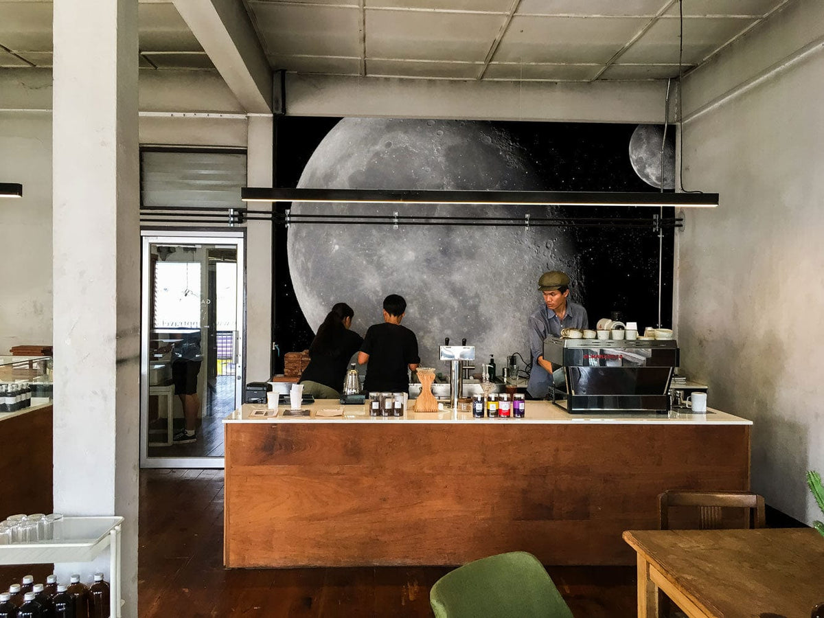 Galaxy Journey Cosmic Moon Mural Wallpaper in café with wooden counter, light walls, and green chair.