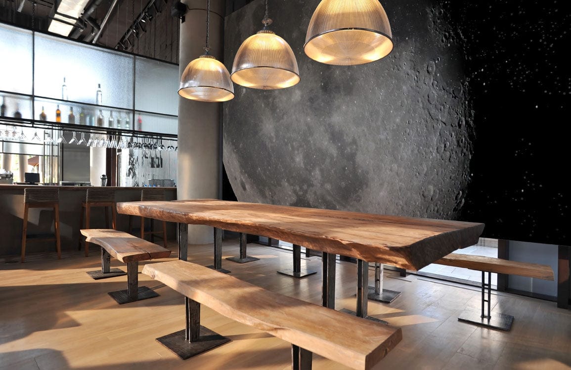 Galaxy Journey Cosmic Moon Mural Wallpaper in dining room, natural wood table, industrial lighting fixtures.