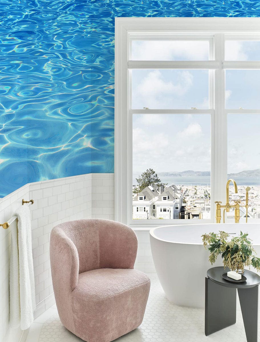Vibrant ocean blue ripple effect mural in bathroom with pink chair, white tub, and golden faucet.