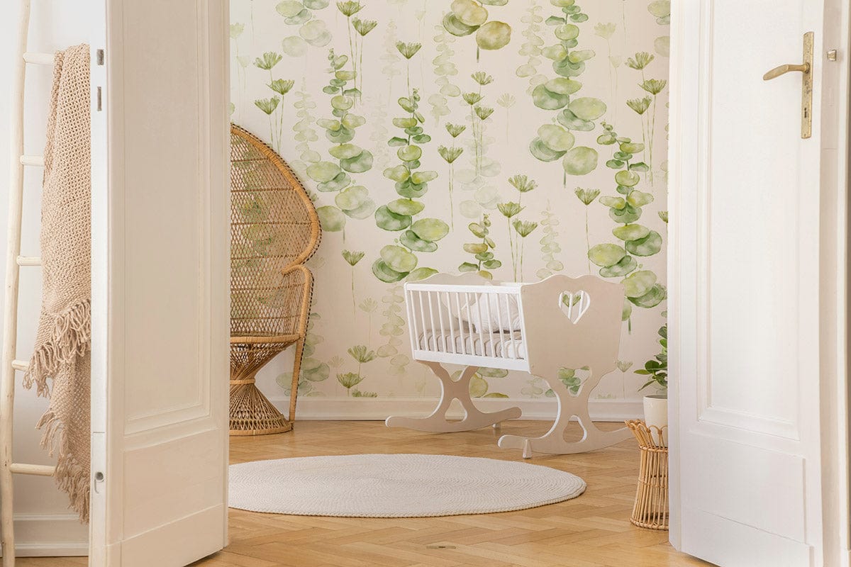 Tranquil wallpaper with eucalyptus design, white crib, wicker chair, wooden flooring in nursery setting.