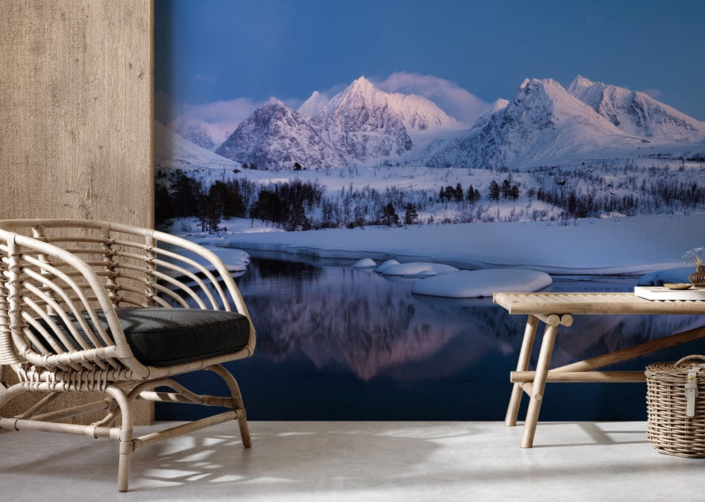 Serene snowy mountain mural in cool blue tones, wicker chair, wooden table, concrete flooring.