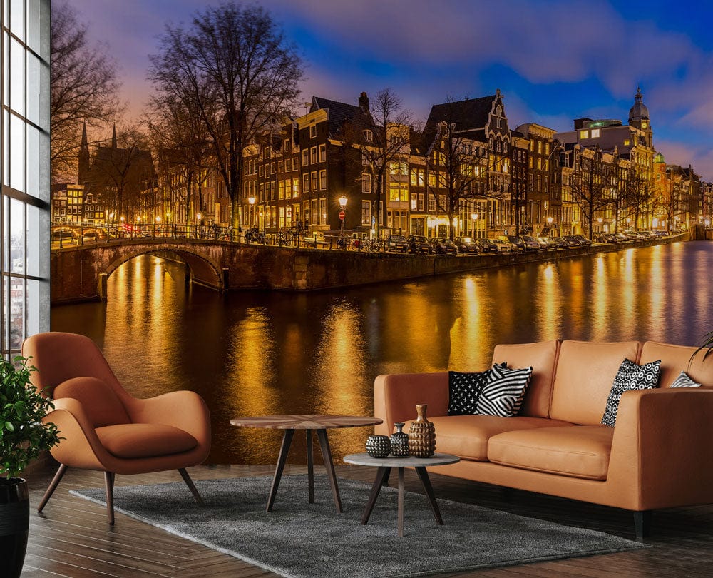 Warm urban mural wallpaper depicting Amsterdam canal evening glow; features tan sofa, modern armchair, grey rug.