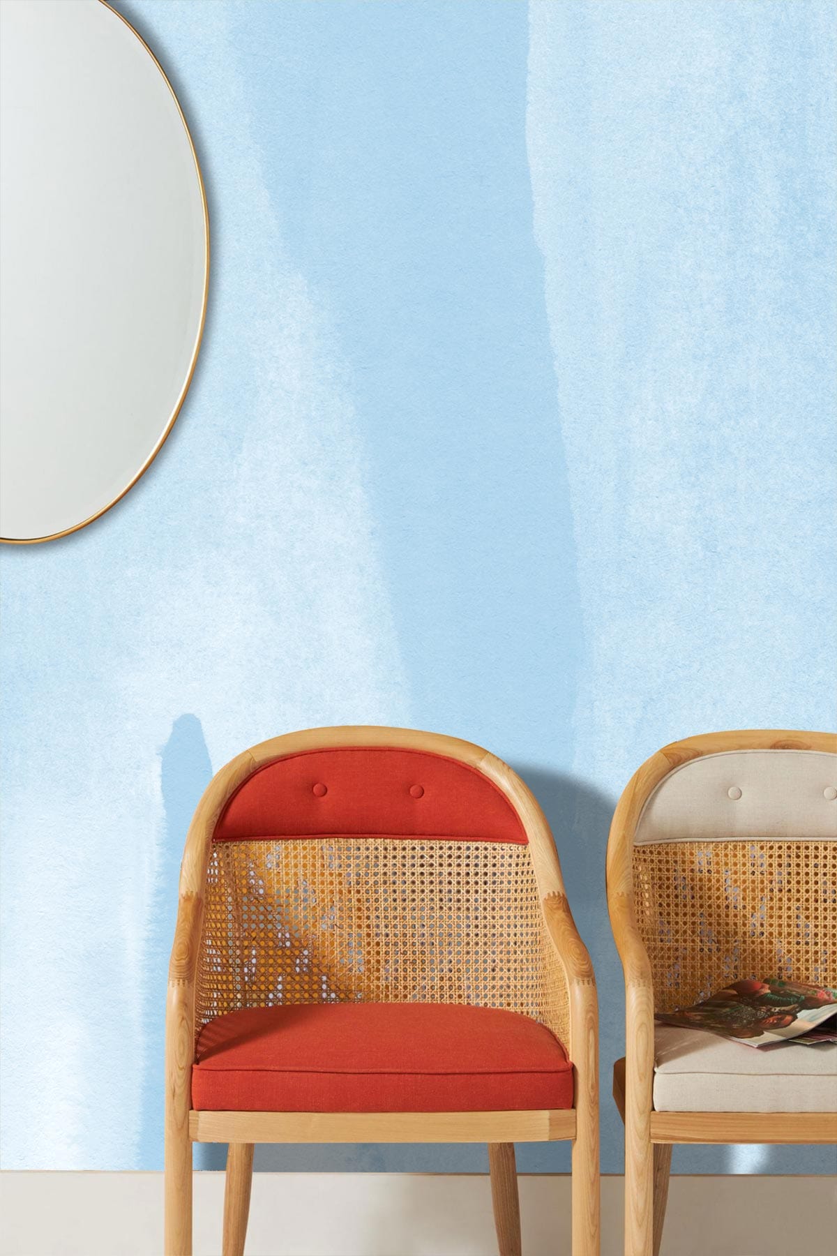 Soft blue watercolour stripe wallpaper, oval mirror, textured walls, wicker chairs, tranquil interior decor.