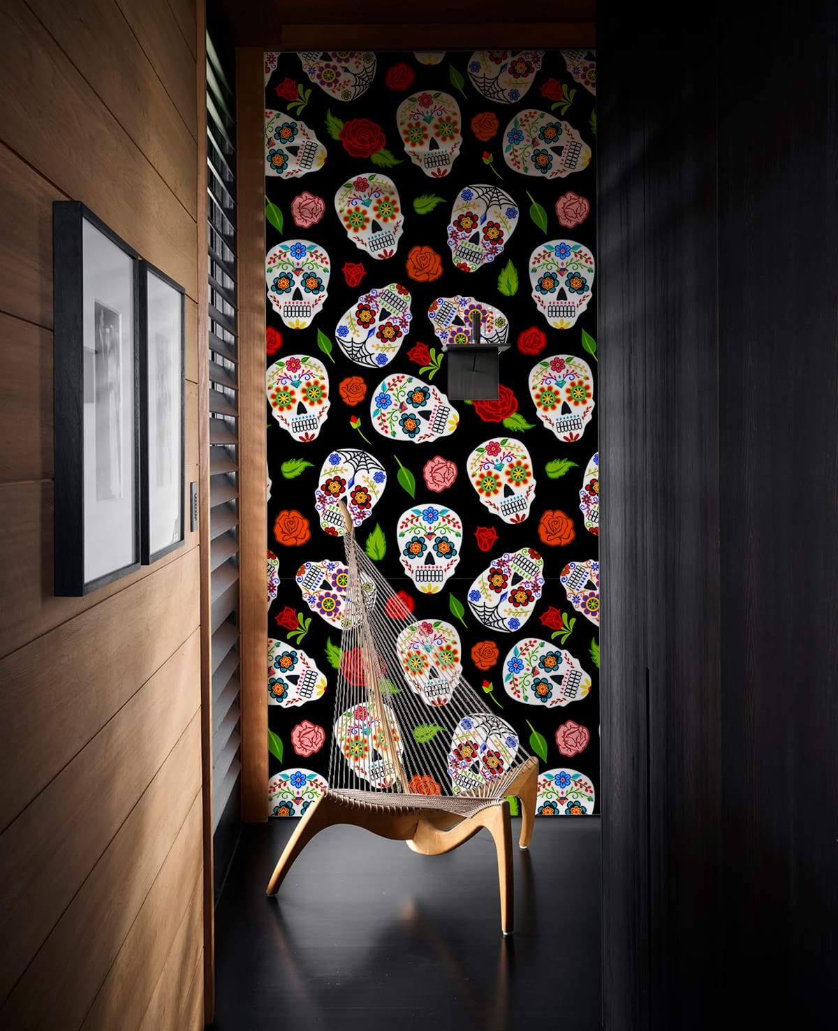 Vibrant sugar skulls and roses patterned black wallpaper, modern chair, wooden walls, dark flooring.