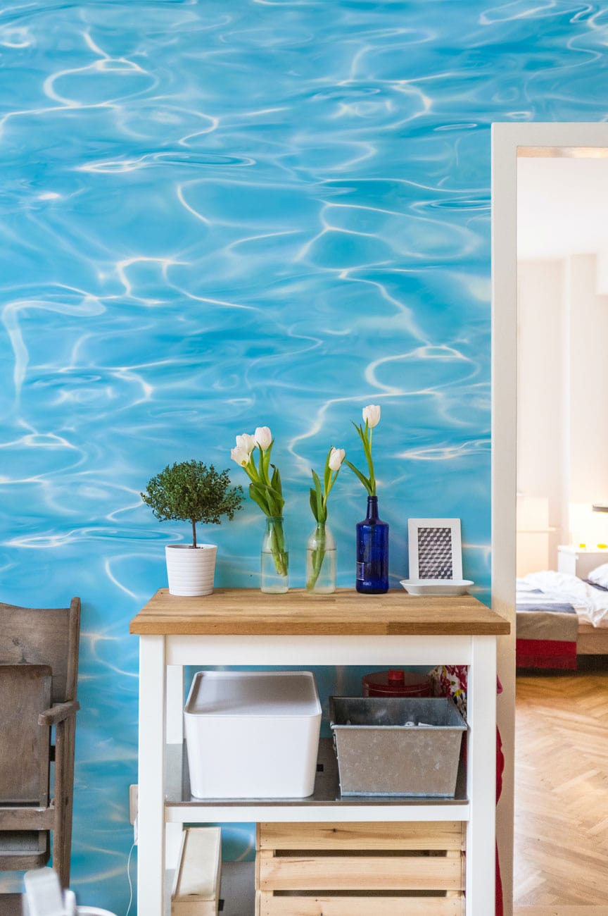 Serene Aqua Ripple wallpaper in room with wooden table and chair, enhancing tranquil interior design.